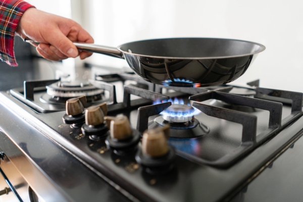 hand holding a pot on top of a blue flame from a propane powered stove
