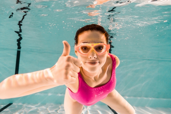 woman making a thumbs up sign while under the pool