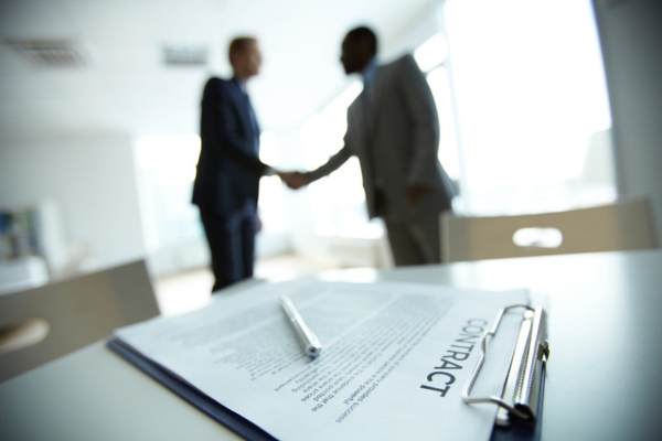 two men shaking hands in the background with a contract on a clipboard on top of a table